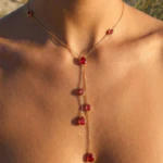 Collier doré femme en Y à gouttes rouges pendantes porté au cou, vue rapprochée au soleil