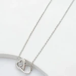 Collier cœurs entrelacés argenté posé sur fond blanc, un cœur serti de petits strass