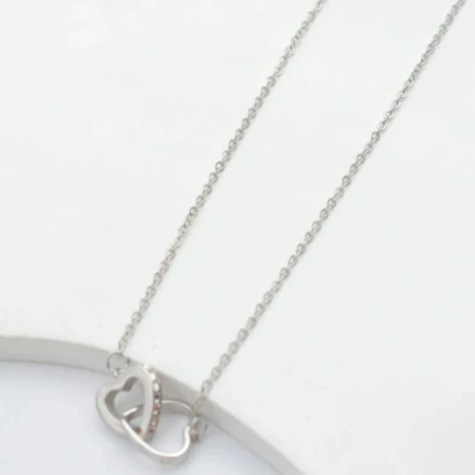 Collier cœurs entrelacés argenté posé sur fond blanc, un cœur serti de petits strass