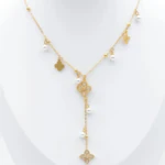 Collier doré à chute centrale, trèfle ajouré, petits charms dorés et perles blanches présenté sur un buste blanc