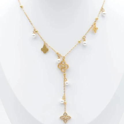 Collier doré à chute centrale, trèfle ajouré, petits charms dorés et perles blanches présenté sur un buste blanc