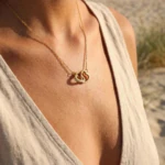Collier doré femme à pendentif cœurs entrelacés serti de strass, porté au cou à la plage
