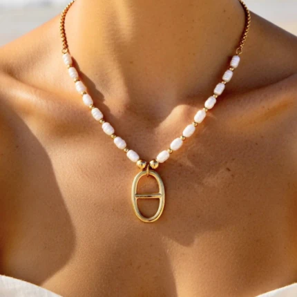 Collier doré femme à perles blanches et pendentif ovale ajouré, porté au cou en plein soleil