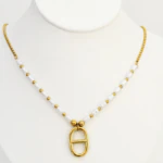 Collier perles blanches et perles dorées à pendentif ovale à barrette, présenté sur un buste blanc