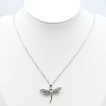 Collier argenté femme à pendentif libellule aux ailes ajourées serties de strass, sur buste blanc