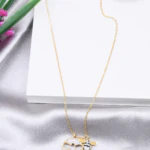 Collier doré femme à pendentif rond pavé de strass, trèfle ajouré et breloque abeille, posé sur satin gris