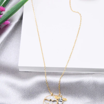 Collier doré femme à pendentif rond pavé de strass, trèfle ajouré et breloque abeille, posé sur satin gris