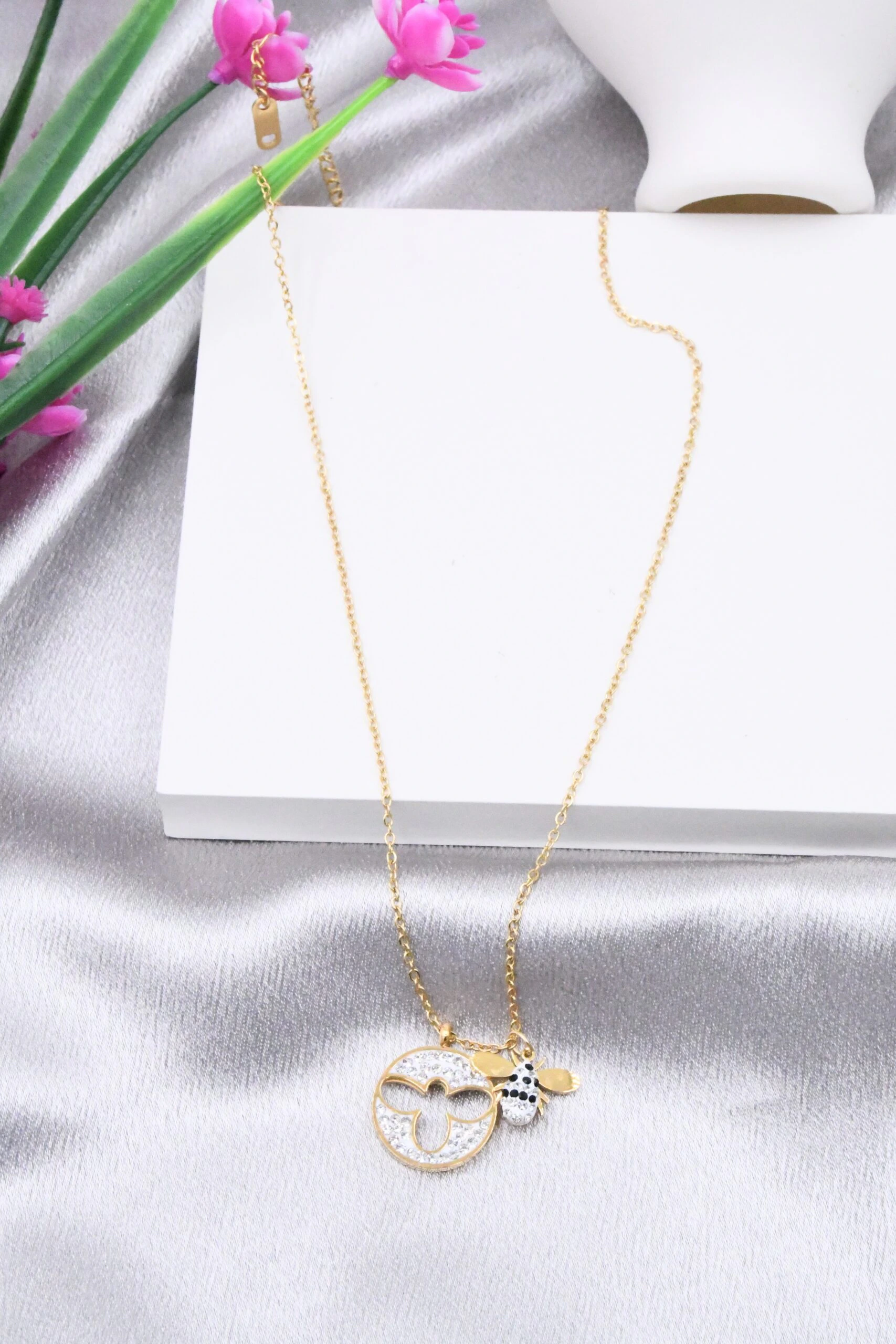 Collier doré femme à pendentif rond pavé de strass, trèfle ajouré et breloque abeille, posé sur satin gris