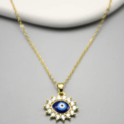 Gros plan du pendentif œil protecteur bleu nuit cerclé de pierres claires sur chaîne fine dorée