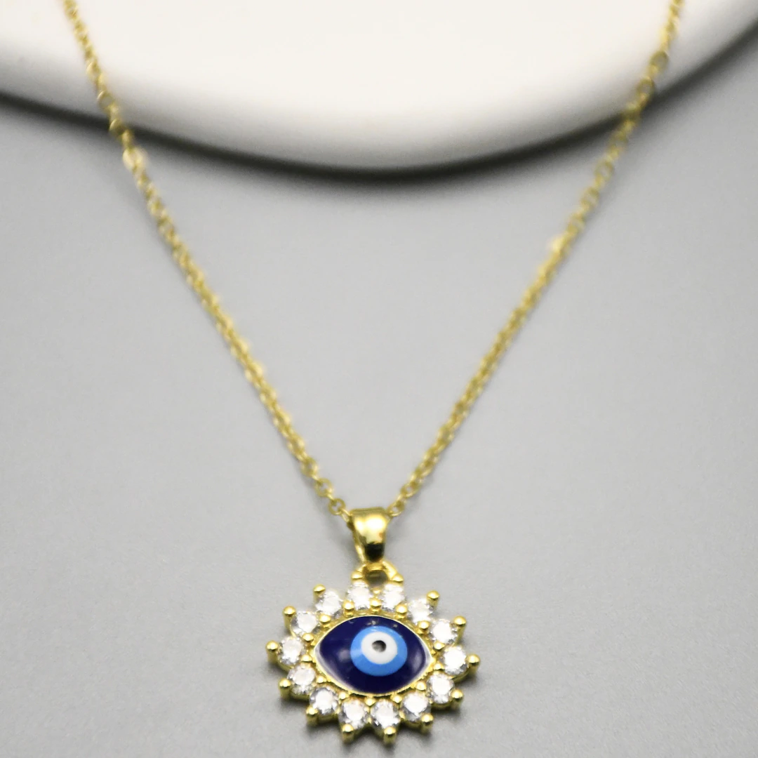 Gros plan du pendentif œil protecteur bleu nuit cerclé de pierres claires sur chaîne fine dorée