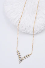 Collier doré femme à motif feuillage en V serti de pierres claires, posé près d'un décor blanc