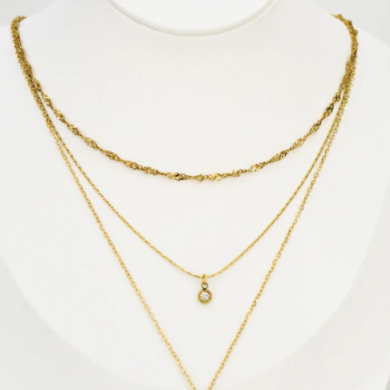 Collier trois rangs doré sur buste blanc : chaîne torsadée, pendentif rond à strass et ovale ajouré