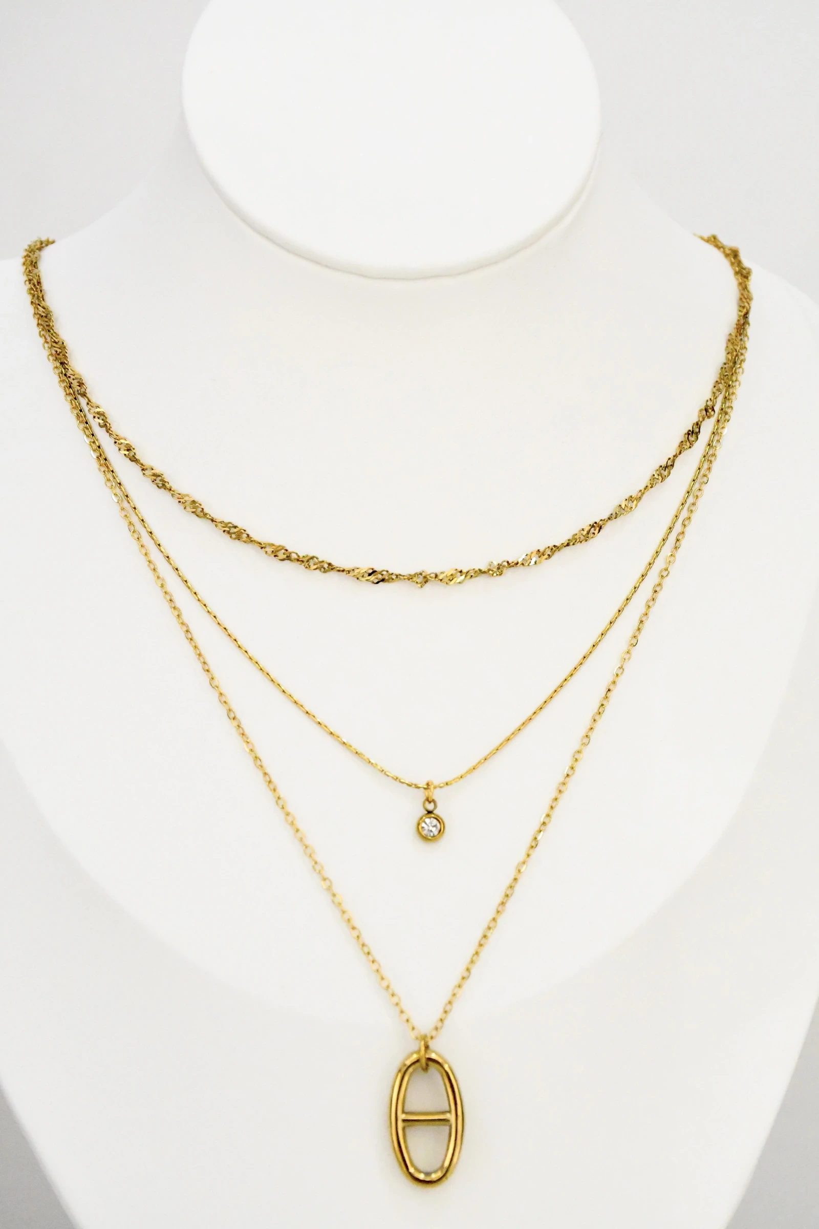 Collier trois rangs doré sur buste blanc : chaîne torsadée, pendentif rond à strass et ovale ajouré