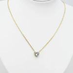 Collier doré femme à petit pendentif cœur en pierre claire facettée, présenté sur un buste blanc