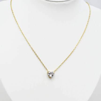 Collier doré femme à petit pendentif cœur en pierre claire facettée, présenté sur un buste blanc