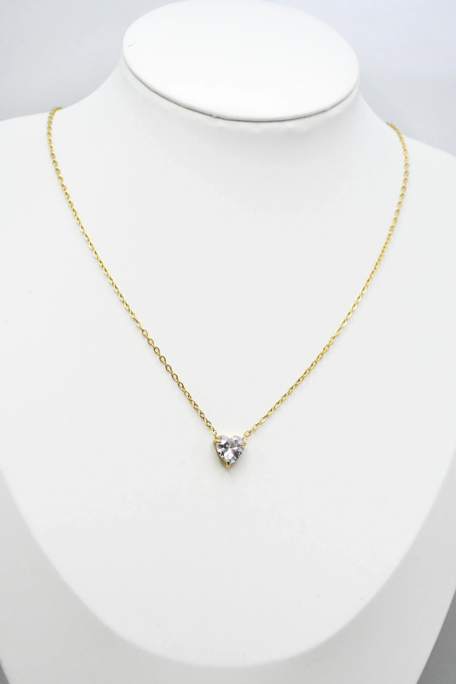 Collier doré femme à petit pendentif cœur en pierre claire facettée, présenté sur un buste blanc