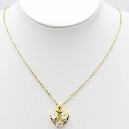 Collier doré femme à pendentif cœur orné de petites fleurs blanches en relief, présenté sur un buste