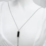 Collier sautoir argenté femme à pendentif rectangulaire noir et deux barrettes pendantes, sur mannequin blanc