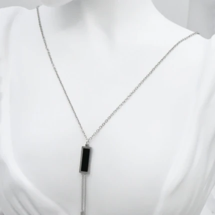 Collier sautoir argenté femme à pendentif rectangulaire noir et deux barrettes pendantes, sur mannequin blanc