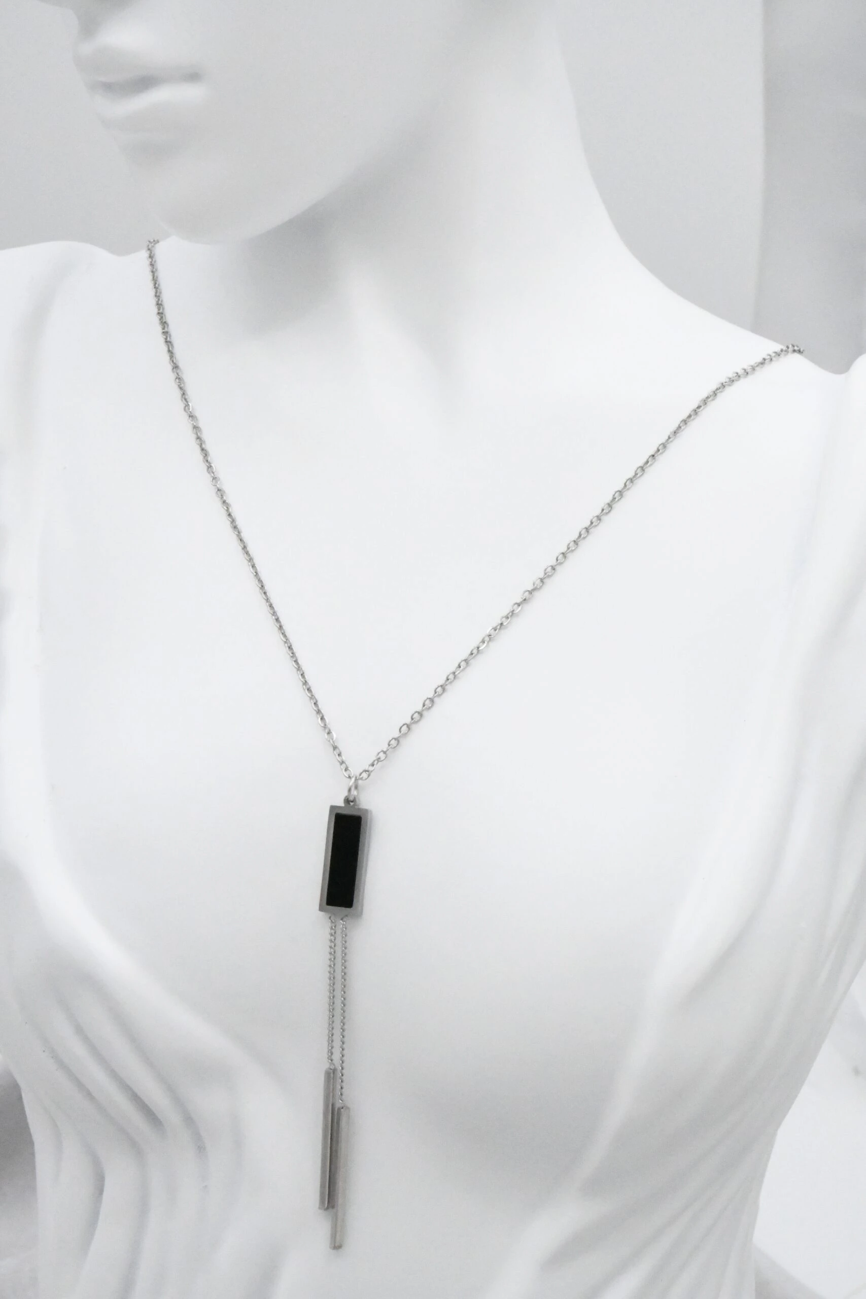 Collier sautoir argenté femme à pendentif rectangulaire noir et deux barrettes pendantes, sur mannequin blanc