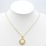Collier doré femme à pendentif carré blanc nacré entouré de strass baguettes, présenté sur un buste
