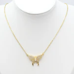 Collier doré femme à pendentif papillon pavé de strass et petites perles blanches, sur buste blanc