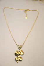Collier chaîne serpent dorée à pendentif ondulé sculptural posé à plat sur fond beige