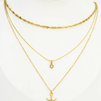 Collier trois chaînes dorées sur buste blanc : maille torsadée, petit pendentif rond et étoile en strass