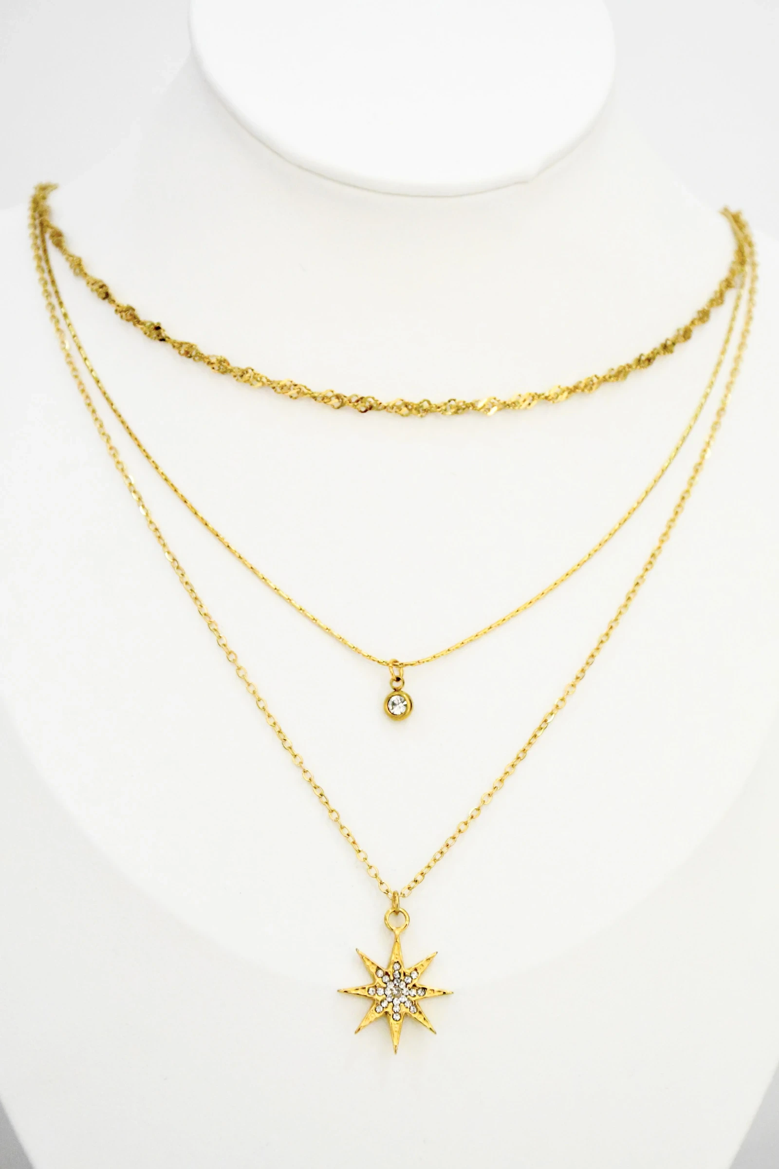 Collier trois chaînes dorées sur buste blanc : maille torsadée, petit pendentif rond et étoile en strass