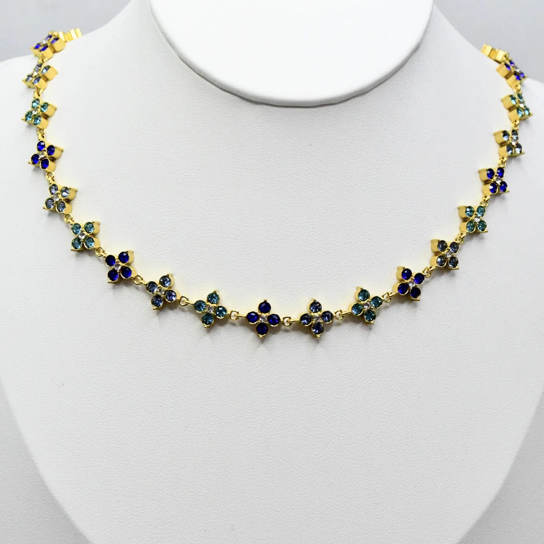 Collier doré femme à maillons trèfles sertis de strass bleu nuit et bleu-vert, présenté sur un buste blanc