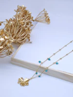 Collier chaîne fine dorée à perles bleu turquoise et fleur dorée posé près de fleurs séchées