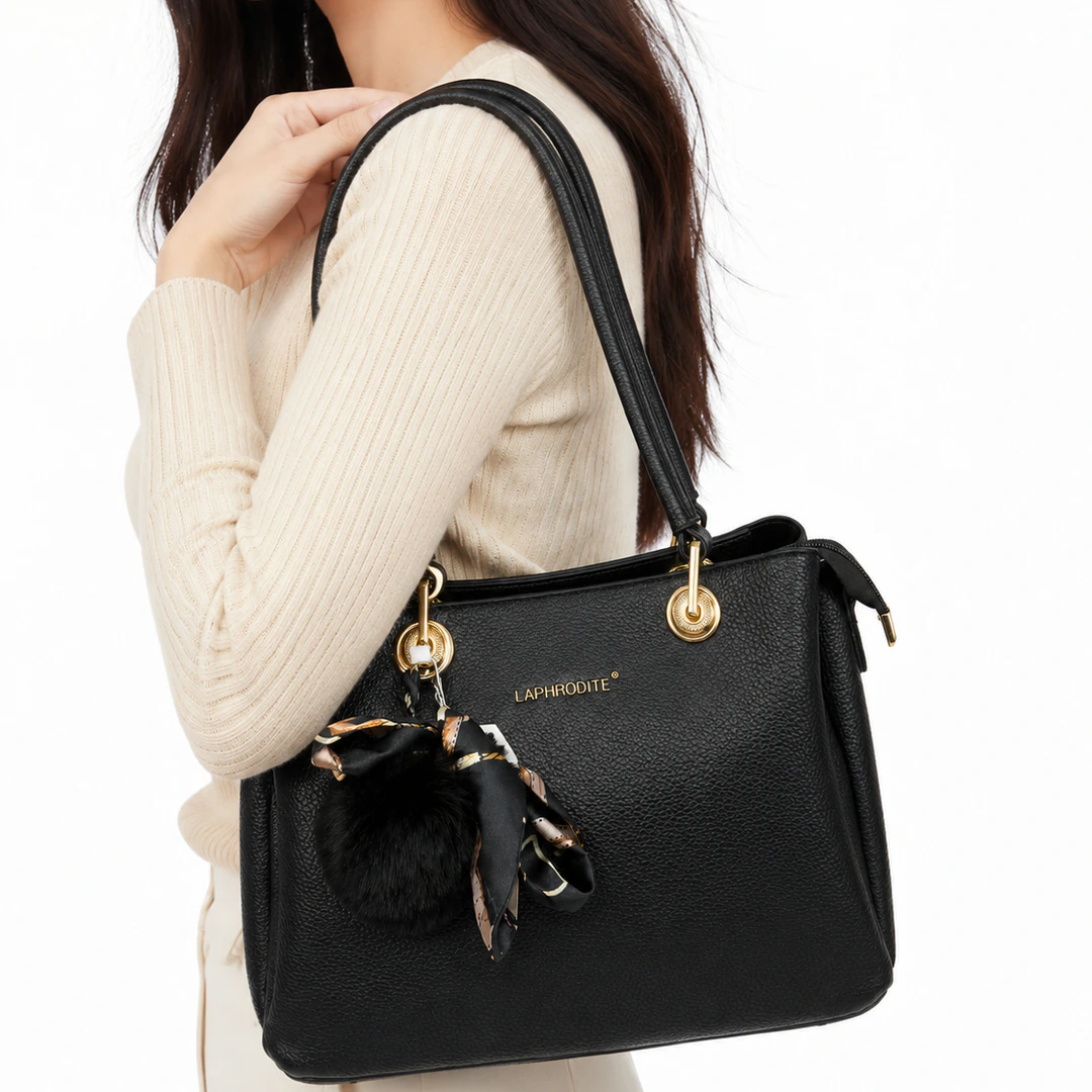 Femme portant le sac à main noir grainé à l'épaule, pompon et foulard accrochés à l'anse