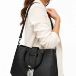 Femme portant à l'épaule le sac à main noir à détail effet serpent, avec une veste crème