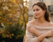 Woman wearing layered gold jewelry and beige sweater outdoors in autumn